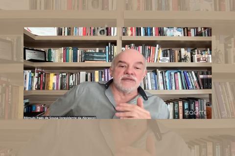 Homem gesticula tendo com fundo uma estante de livros