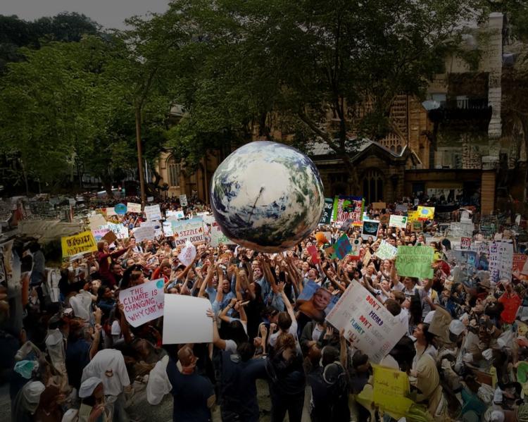 Foto: OMS Uma multidão de pessoas está com os braços erguidos apontando para uma esfera que simula o planeta terra