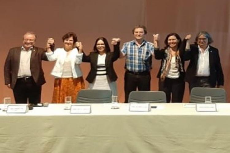 Homens e mulheres lado a lado erguem os braços de mãos dadas e sorriem
