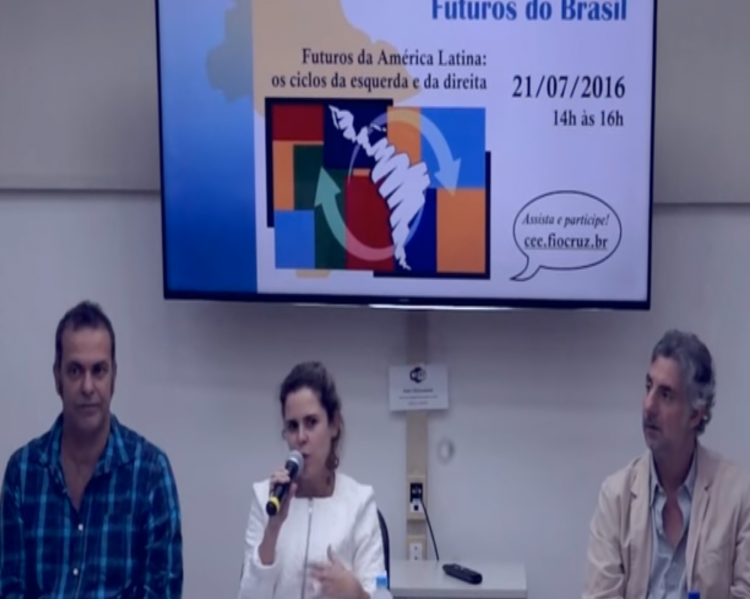 Palestrantes, dois homens nas pontas, uma mulher ao centro, à mesa de debates