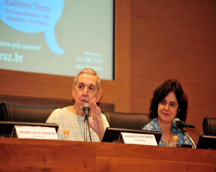 Wanderley Guilherme (homem grisalho em mesa de debate, gesticulando, ao lado de uma mulher de cabelos pretos, Nísia Trindade)