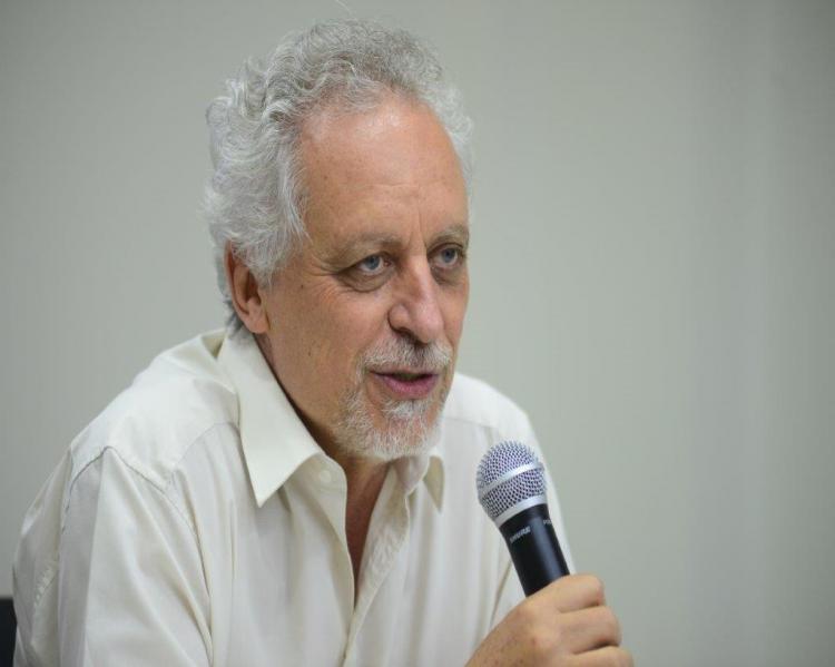 Homem grisalho de camisa branca fala ao microfone