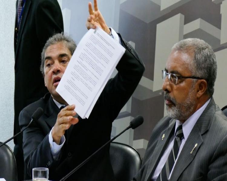 Homem à esquerda mostra uma folha de papel observado por um homem à direita. Ambos de ternos escuros.