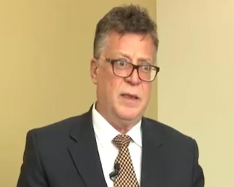 Homem de óculos e terno em close, com microfone na lapela