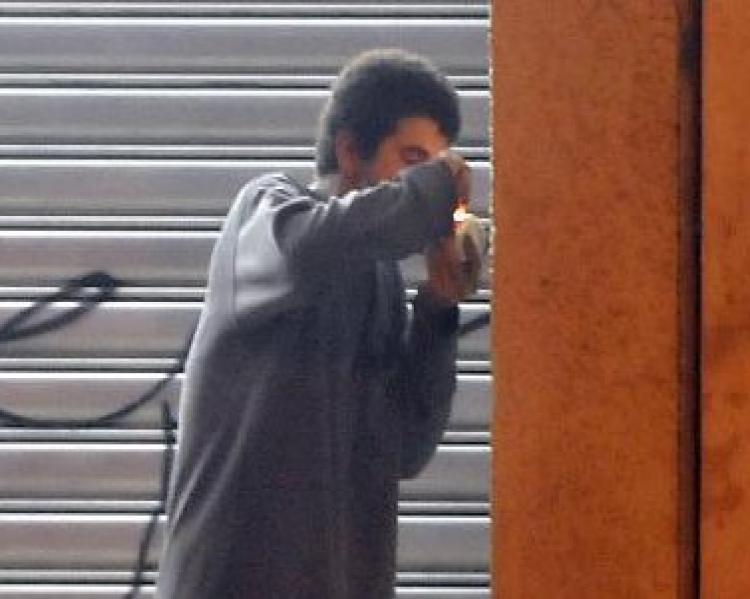 Homem de perfil, vestindo camiseta de manga comprida cinza, próximo a uma pilastra, usando crack