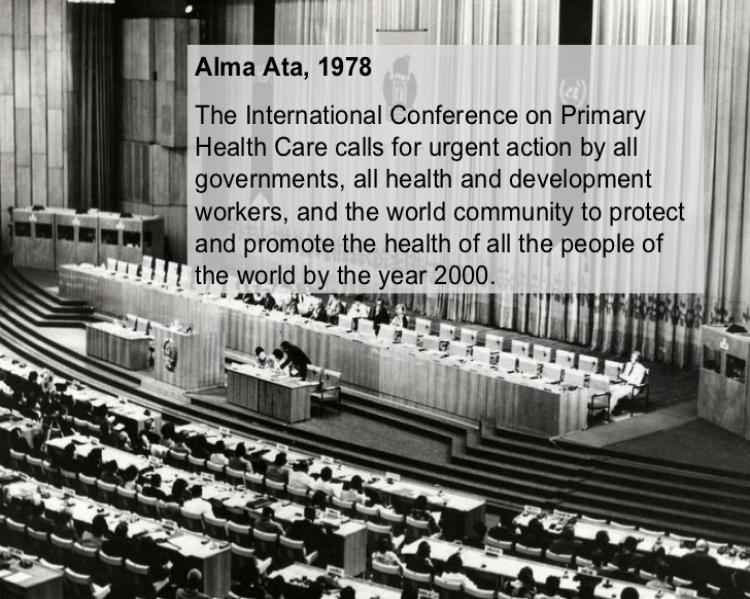 foto antiga em preto e branco mostra uma plenária vista do alto, com um palco à frente e pessoas na mesa de debates