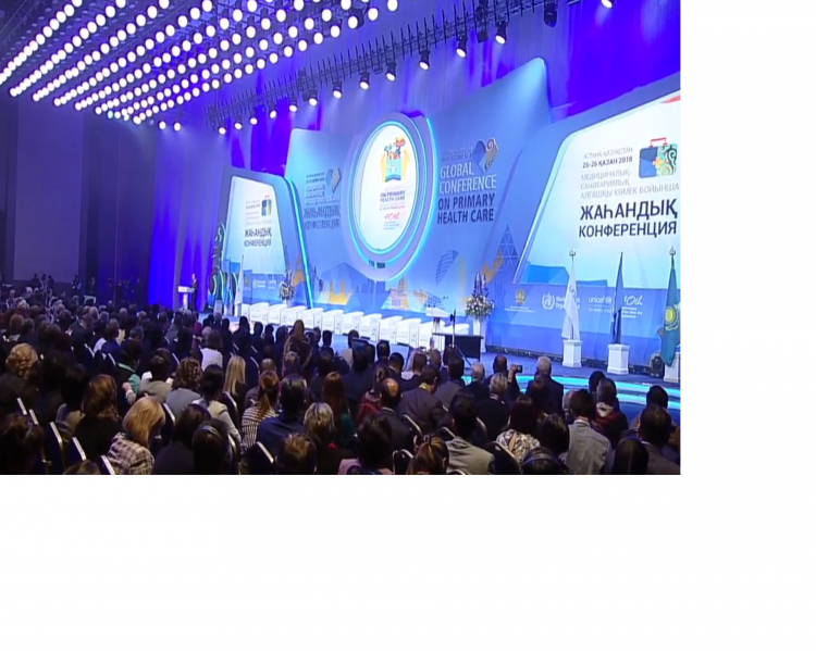 Plenária vista de cima, auditório lotado e grande mesa no palco, com projeção em lilás atrás, indicando o nome da conferência