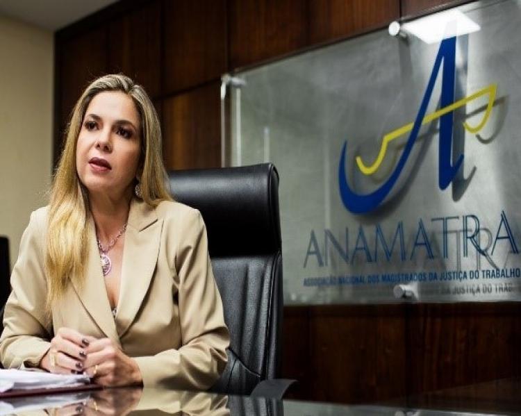 Mulher loura de blaser claro, em uma mesa, fala e gesticula