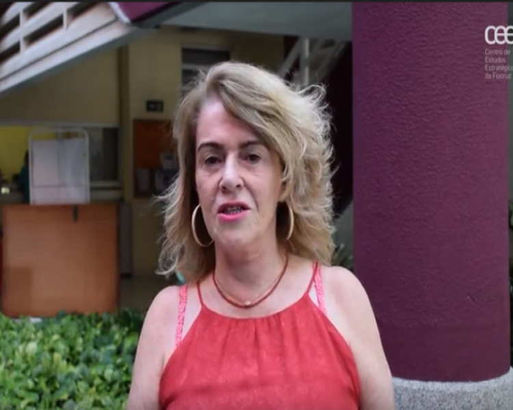 Mulher loura, com vestido vermelho de alças, em primeiro plano, falando