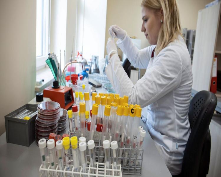 Mulher de jaleco branco manipula tubos ensaios sentada em uma bancada de laboratório