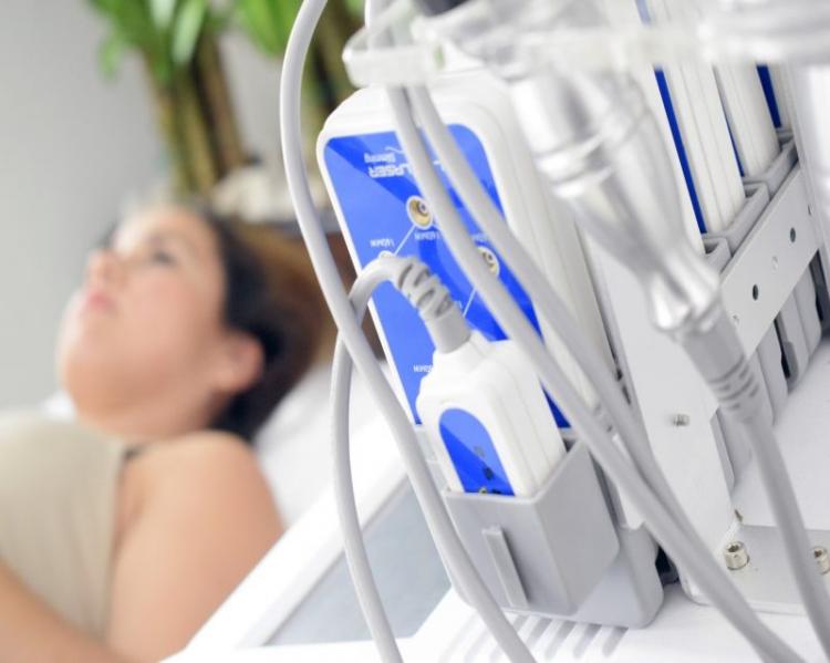 Mulher deitada em maca, tendo em primeiro plano tomadas e fios, para realização de ultrassonografia