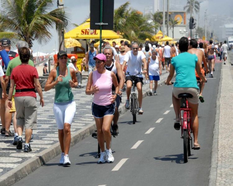 Pessoas caminhando, correndo e andando de bicicleta no calçadão de uma orla