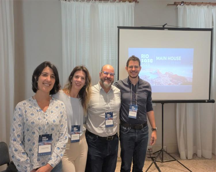 Duas mulheres e dois homens, lado a lado, sorriem para a foto, tendo um telão ao fundo, onde se lê o nome do evento Rio Sase 2023