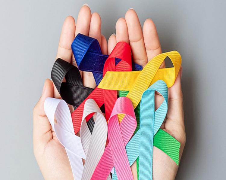 Mãos em concha seguram fitinhas coloridas relativas à prevenção do câncer