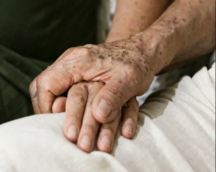 Duas mãos apoiadas uma sobre a outra, uma delas de pessoa idosa