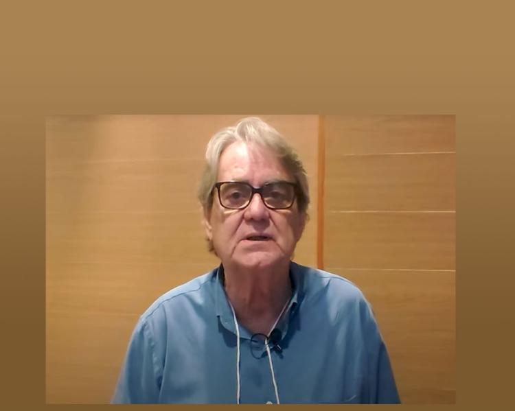 Homem de camisa azul e óculos olha para a câmera e fala