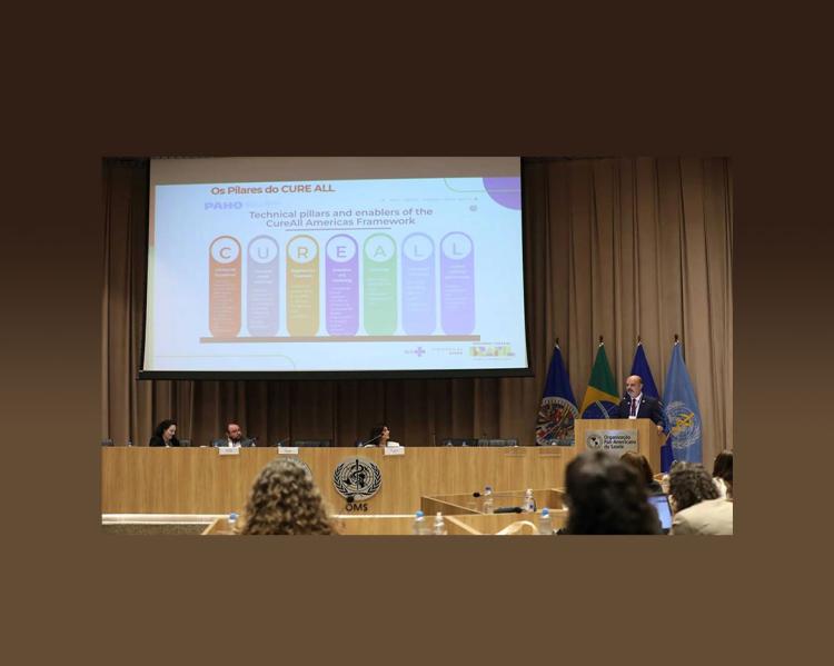 Mesa de debate com duas mulheres e um homem, mais um homem no púlpito, falando. No telão imagem da iniciativa Cure All