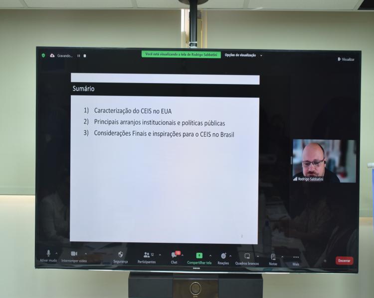 Telão com imagem do pesquisador à esquerda e tela de sua apresentação à direita