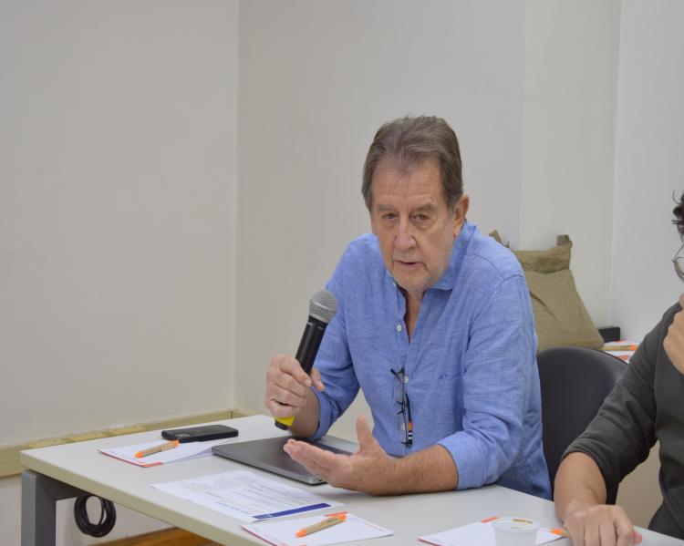 Homem fala ao microfone em uma mesa de debate