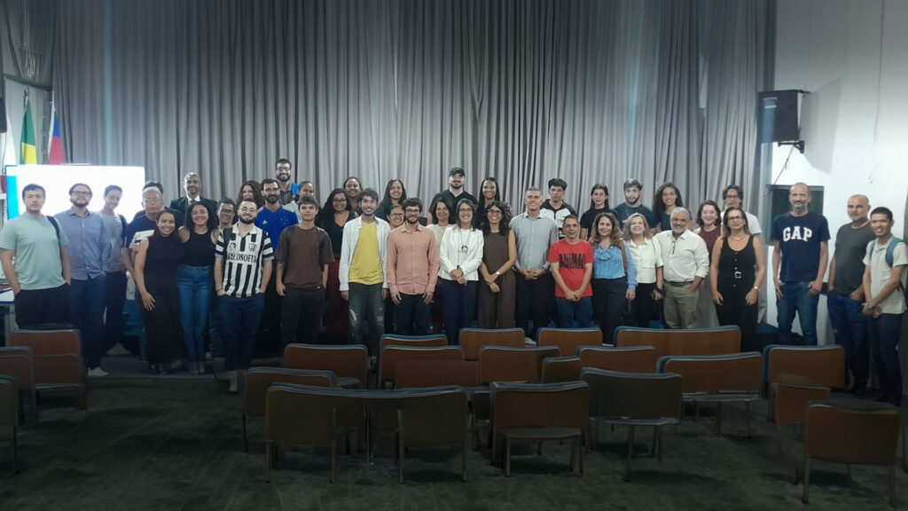 Homens e mulheres, jovens e adultos, estudantes e professores, estão de pé e sorriem, após aula inaugural