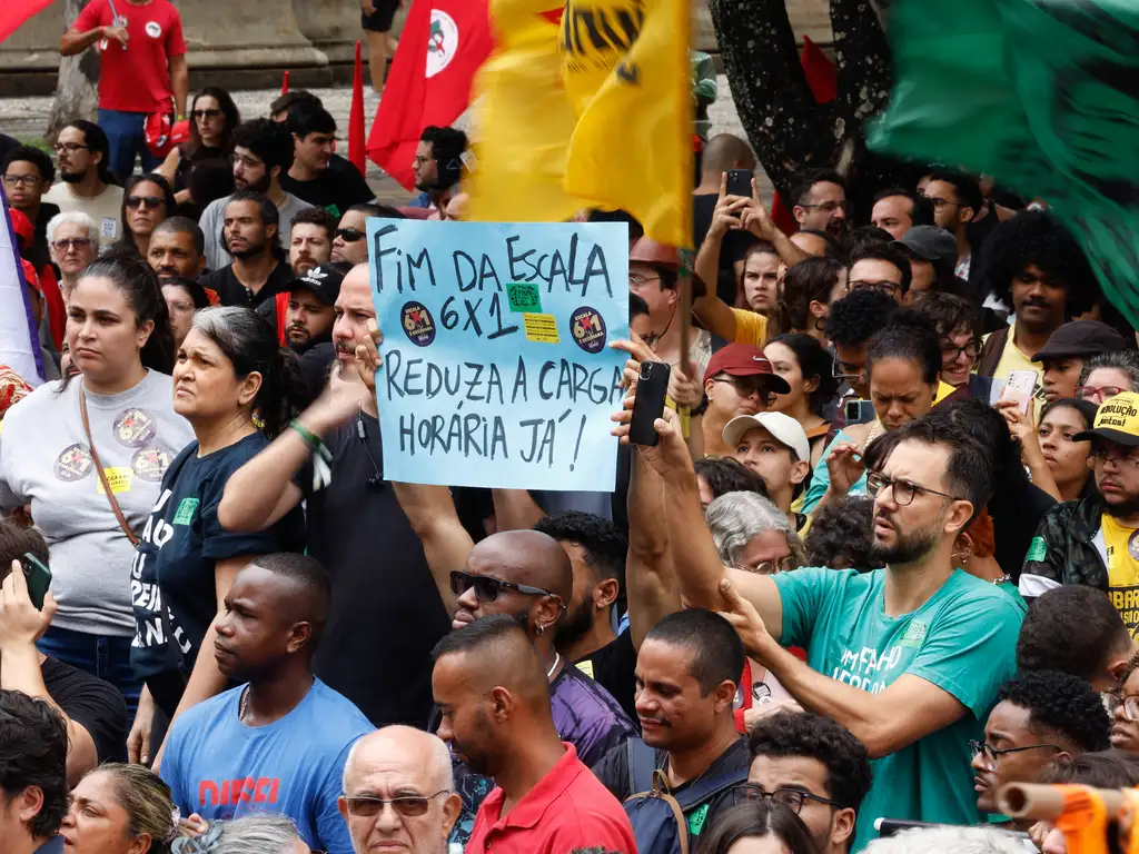 Homens e mulheres em manifestação, seguram cartaz em que se pede o fim da escala 6x1